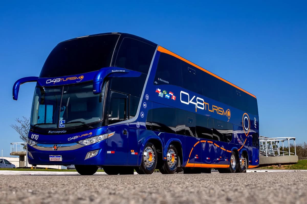 Ônibus Double Decker azul e laranja da 048 Turismo sob céu azul