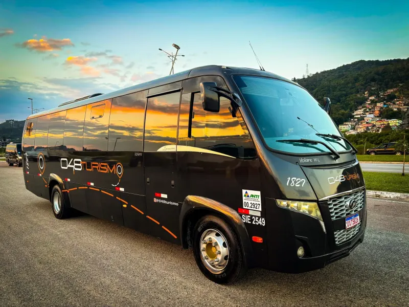 Micro-ônibus preto da 048 Turismo com o pôr do sol refletido na lataria